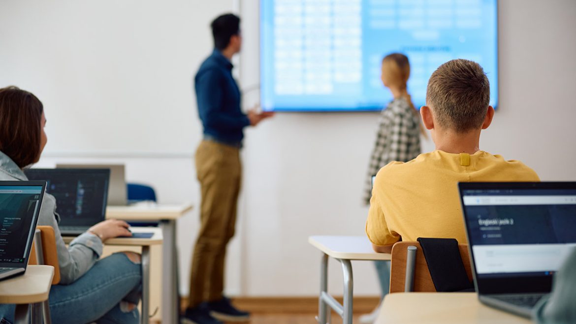 Um professor sorri enquanto usa um tablet para planejar uma aula, com ícones de ideias e criatividade ao redor, simbolizando o uso da IA para educadores.