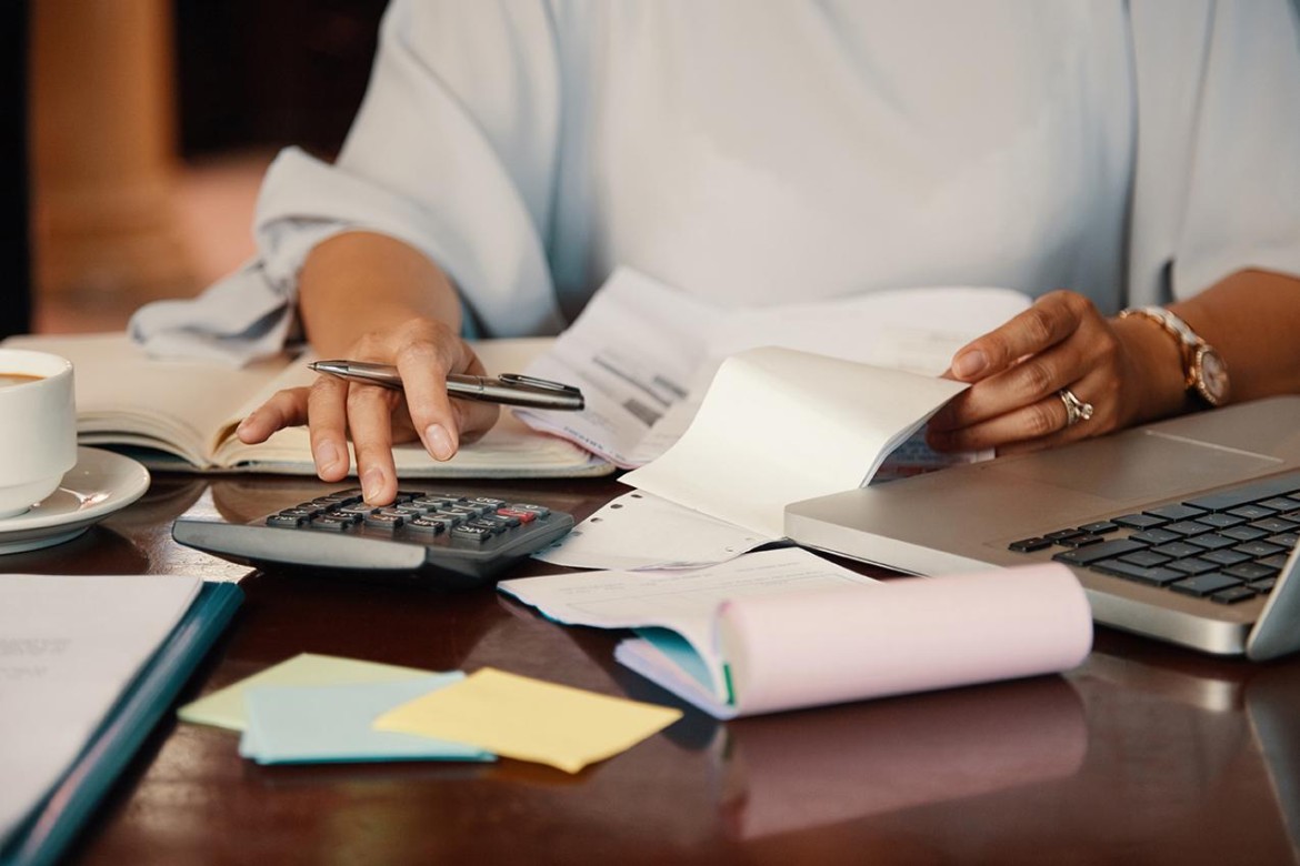 Uma pessoa olha pensativa para uma calculadora, com um ícone de IA ao lado, antes de fazer uma compra, simbolizando o cálculo do impacto de uma compra parcelada no orçamento.